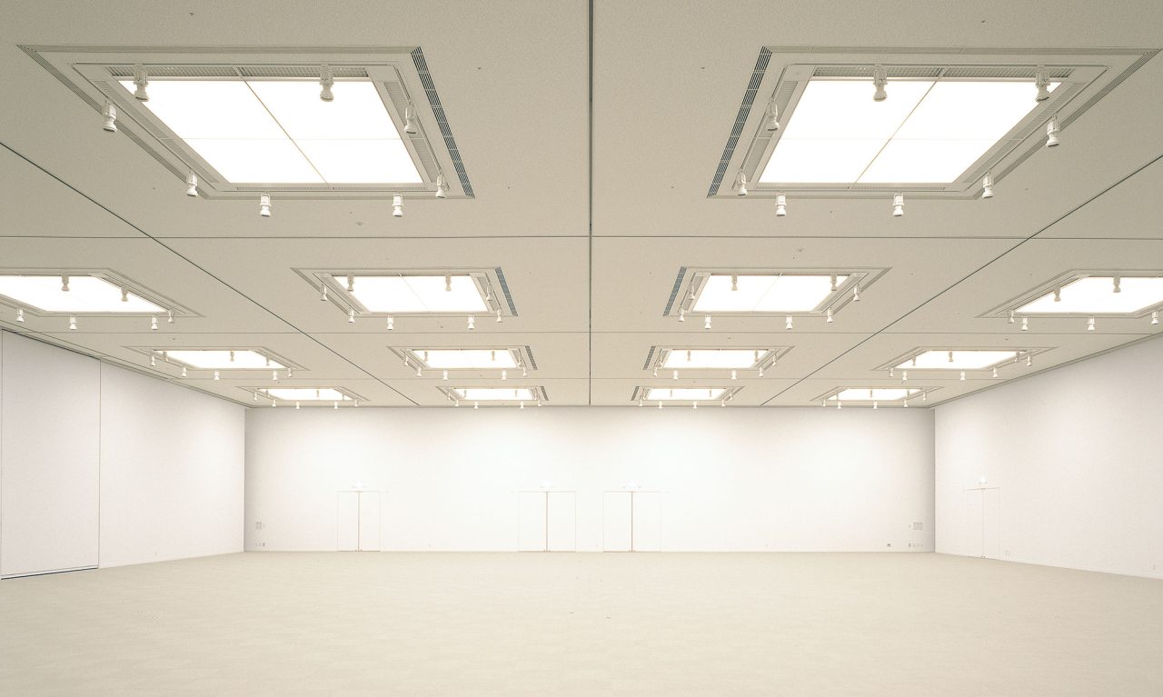 写真：白い壁、ライトグレーの床と天井の展示室。天井に移動壁のレールがある