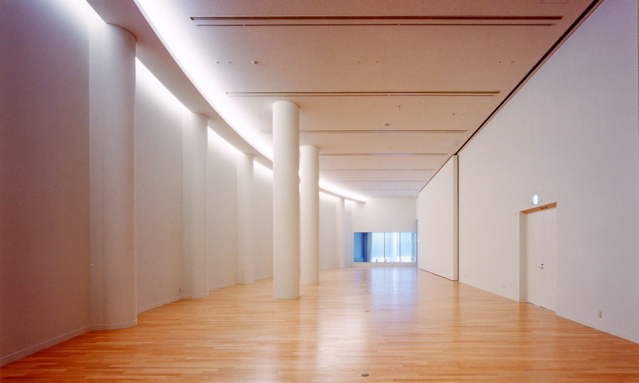 写真：奥に向かってカーブを描くスペース。フローリングの床に白い壁。壁上部の曲面に沿って間接照明が光っている。